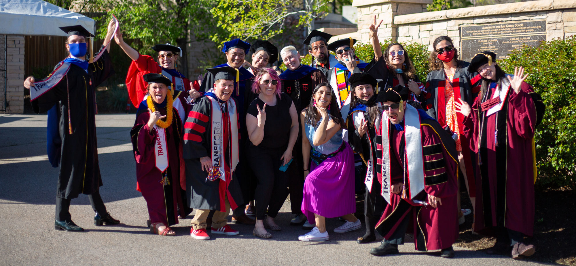 a group of Transform staff and faculty do a silly group photo in their graduation regalia at the Red Butte Gardens