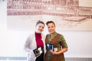 Rosa Pimentel and Dr. Andrea Baldwin standing next to each other, smiling at the camera. Each holds a black and gold award plaque