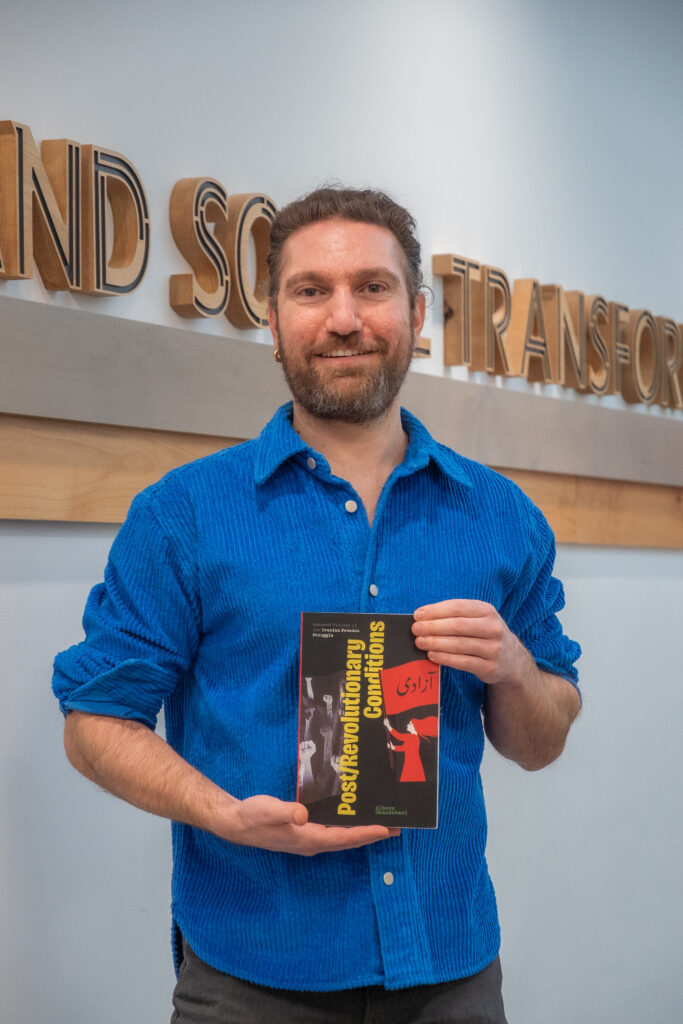 Dr. Alborz Ghandehair, a middle aged male professor, holds a copy of his new book as if on display